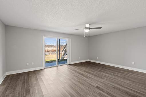 A living room with a ceiling fan and sliding glass doors leading to a deck at Mandarin Bay Apartments.