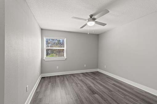 A bedroom with a ceiling fan and a window with a view of trees at Mandarin Bay Apartments.