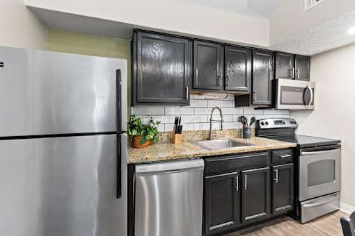 A kitchen with black cabinets and a stainless steel refrigerator.
