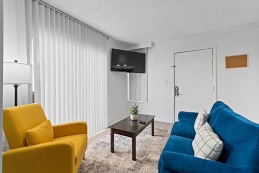 A living room with a yellow chair, a blue couch, and a flat screen TV mounted on the wall.
