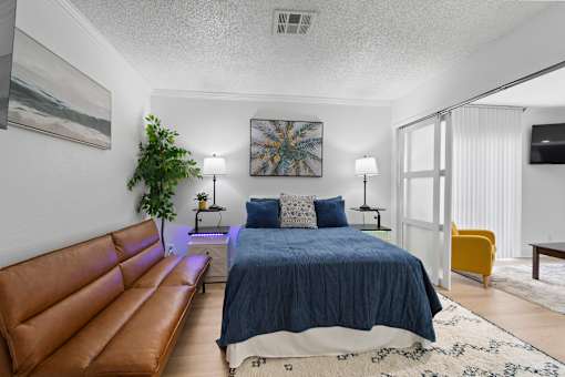 A bedroom with a blue bedspread and a brown leather couch.