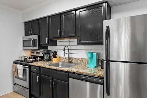A kitchen with black cabinets and a stainless steel refrigerator.