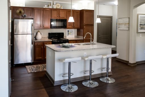 A modern kitchen at Austin Park Apartments in Miamisburg, Ohio features dark brown cabinets, granite-style countertops, an island with barstools, and stainless steel appliances.