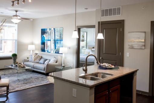The living room in this updated modern interior at Austin Park Apartments in Miamisburg, Ohio showcases hardwood flooring, granite-style countertops, and a kitchen island, welcoming pets.