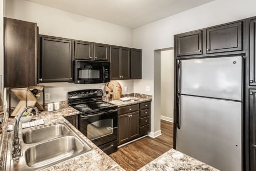 A kitchen equipped with stainless steel and black appliances, granite countertops, dark wood cabinets, and hardwood-style flooring.