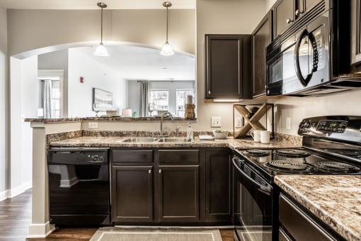 A kitchen at The Fort equipped with dark wood cabinets, black appliances, light fixtures, and hardwood-style flooring.