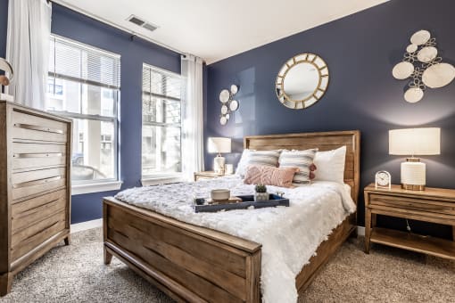 A furnished bedroom with blue walls, carpeted flooring, and a window.