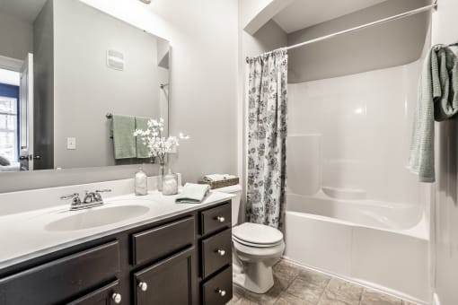 A bathroom with a large vanity and a mirror, and a white tub with white tile walls.