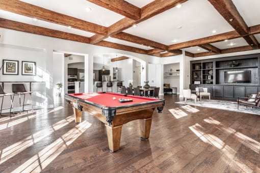A pool table in a gathering space with seating areas and hardwood-style flooring.