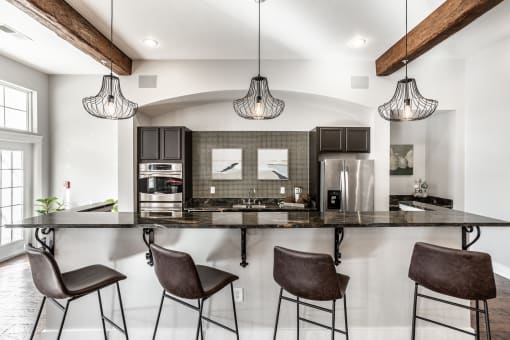 Four bar stools facing a kitchen with stainless steel appliances and light fixtures at The Fort.