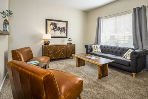 Three-BR Apartments in Pickerington OH - Arbors at Turnberry - Living Room with Large Window Brown Leather Chairs, Blue Sofa, a Coffee Table, and Carpet.