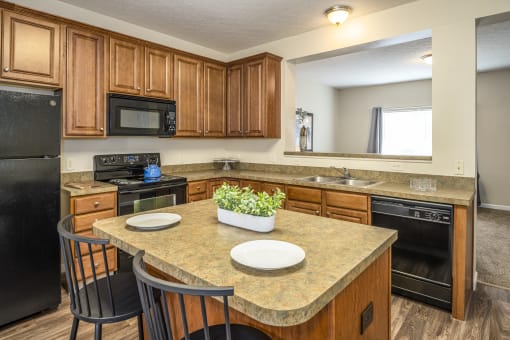 Apartments for Rent in Pickerington - Arbors at Turnberry - Kitchen with a Breakfast Island and Barstools, Light Countertops, Brown Cabinets, and Black Appliances.