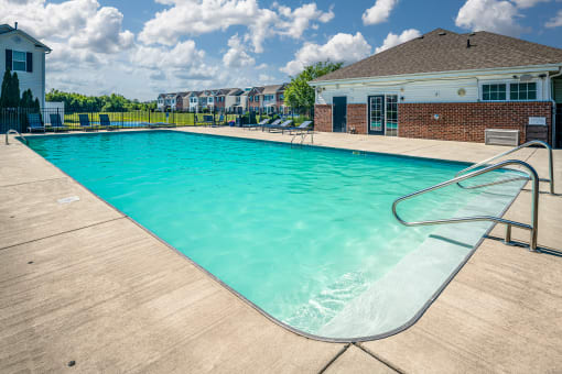 Pet Friendly Apartments in Pickerington, OH - Arbors at Turnberry - Pool with Lounge Chairs, Concrete Deck, and Building in the Background.