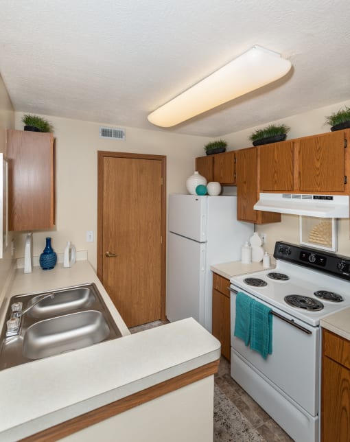 Pet-Friendly Apartments in Hilliard, OH - Residences at Breckenridge - Kitchen with Wood-Style Cabinetry, Electric Stove, Refrigerator, and Dual Sinks.