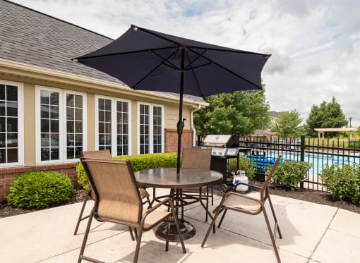 1 BR Apartments in Hilliard, OH - Residences at Breckenridge - BBq Area with Grill, Table, Chairs, and Umbrella Near the Pool.