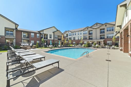 A resort-style swimming pool with a sundeck, lounge chairs, and well-kept landscaping.