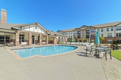 The resort-style swimming pool and sundeck at Austin Park Apartments feature shaded tables and comfortable lounge chairs.