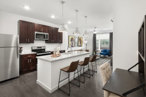 Madisonville Apartments Near Oakley and Hyde Park - Madamore - Kitchen with Dark Wood Cabinets, Granite-Style Countertops, Island with Barstools, and Stainless Steel Appliances.