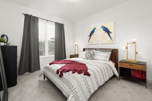 Studio Apartments in Cincinnati, OH - Madamore - Bedroom with Bed, Nightstands, Lamps, Dresser, Carpet Flooring, and Large Window.