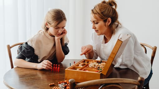 A woman and a girl are playing a board game at a table.