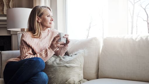 A woman in a pink sweater is sitting on a couch holding a mug.