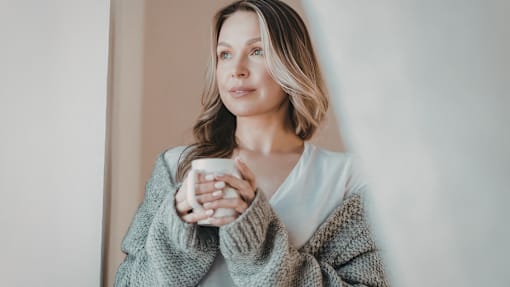 A woman in a grey sweater is holding a white mug.