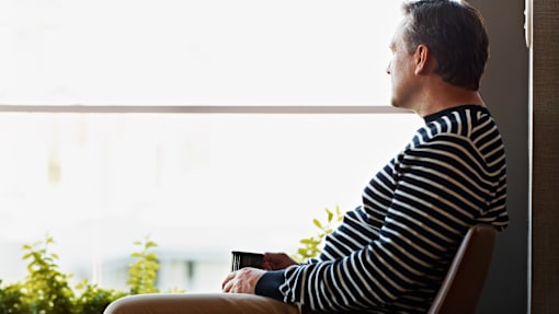 A man in a striped shirt is sitting by a window holding a cup.