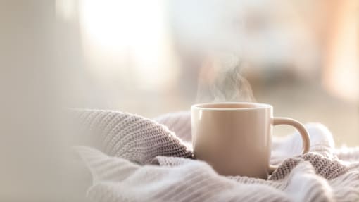 A cup of coffee is steaming on a cozy blanket.