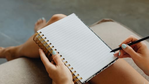 A person is writing in a notebook with a pen.