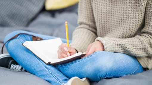 A person is writing in a notebook with a yellow pencil.
