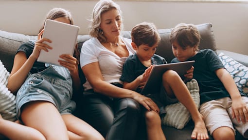 A family of four is sitting on a couch, each using a tablet.