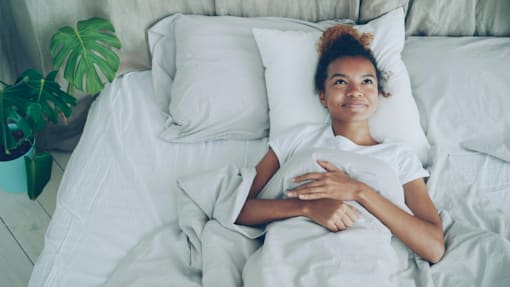 A woman is lying in bed with her hand on her chest.