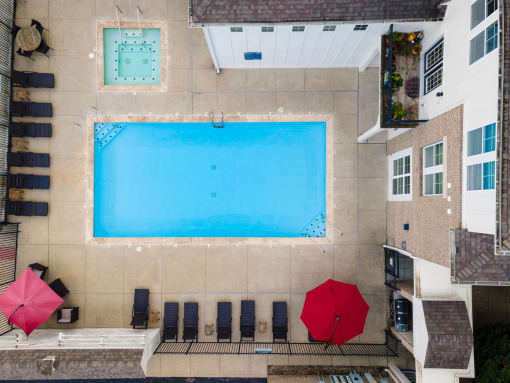 Birds eye view of a swimming pool with lounge chairs and two red umbrellas.