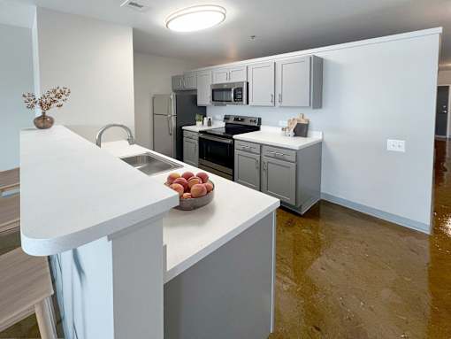 A kitchen with white countertops and a bowl of fruit on it.