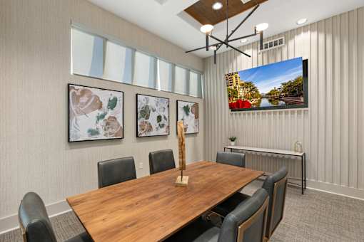 A conference room with a long table and chairs, a television on the wall, and three framed pictures on the wall.
