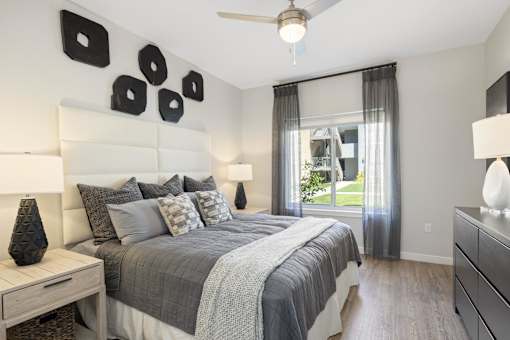 A bedroom with a large bed, a ceiling fan, and a window with curtains.