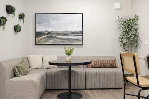 A living room with a grey couch, a round table, and a painting on the wall.