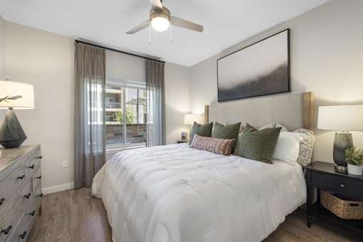 A bedroom with a large bed, a ceiling fan, and a painting on the wall.
