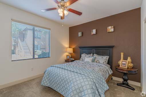 A bedroom with a bed, a ceiling fan, and a window with blinds.