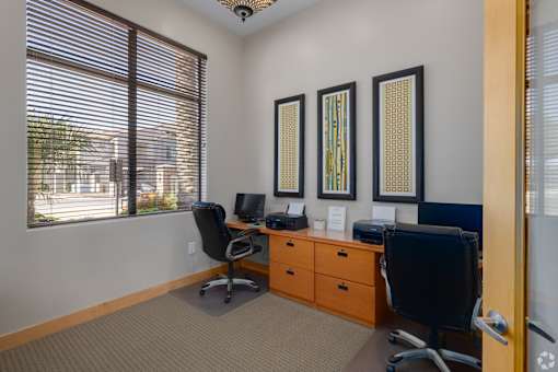 A room with two chairs, a desk, and three framed pictures on the wall.