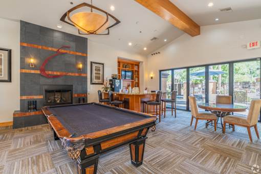 A pool table is in the middle of a room with a fireplace and a bar.