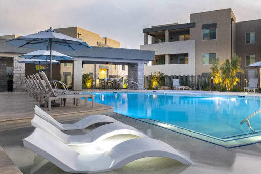 a swimming pool with lounge chairs and umbrellas in front of a building