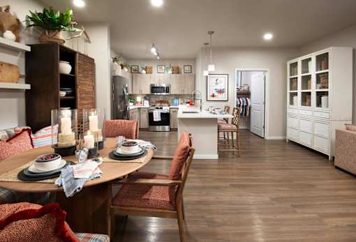 A dining room with a table set for two and a kitchen in the background.