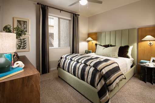 A bedroom with a bed, nightstand, and a plant on a table.