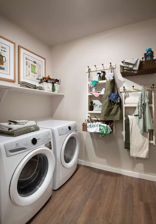 A laundry room with two washing machines and a shelf with hanging clothes.