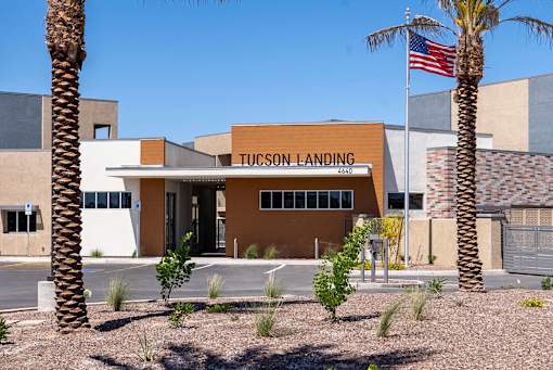 The Tucson Landing building is surrounded by palm trees and has an American flag flying in front.