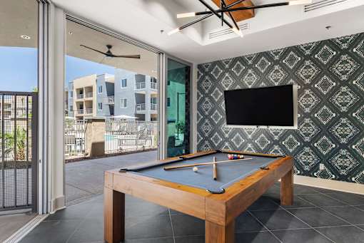 A pool table with a green cloth and a television on the wall.