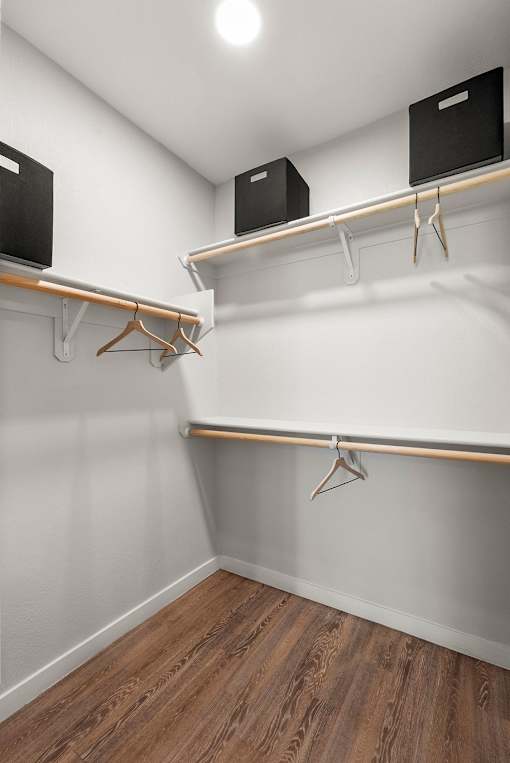 A room with a white wall and a wooden floor with two shelves and two black boxes.