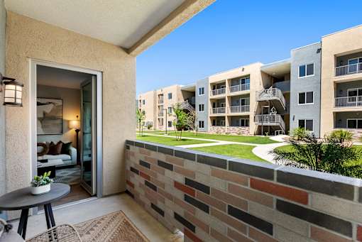 A balcony with a table and chairs overlooks a courtyard with a brick wall.