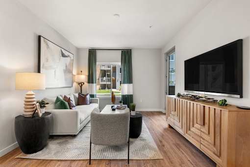 A living room with a white couch, a grey chair, a wooden cabinet, and a flat screen TV.